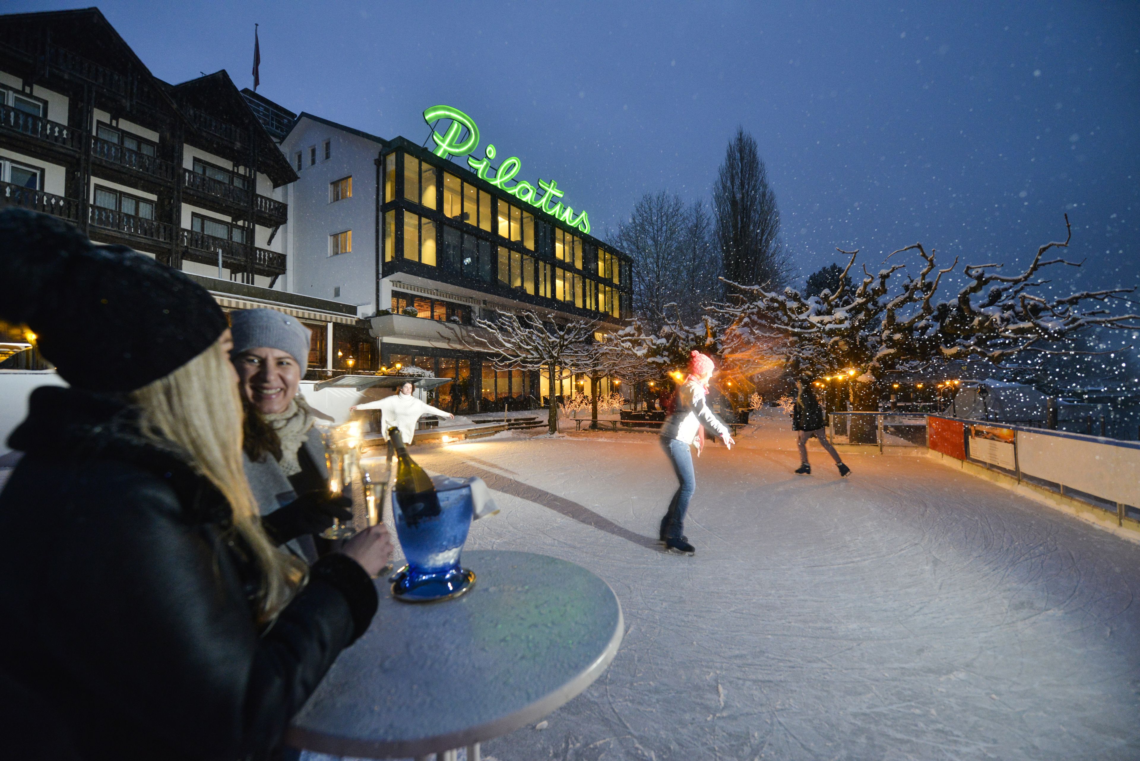 Ein Hotel namens Pilatus mit einer Neonreklame, einem Außenbereich zum Sitzen und verschneiter Umgebung.