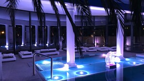 Zona de piscina con sillones reclinables, un jacuzzi y piscina cubierta con paredes de vidrio.