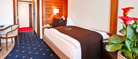 A hotel room with a bed, a desk, a chair, a lamp, and a potted plant.
