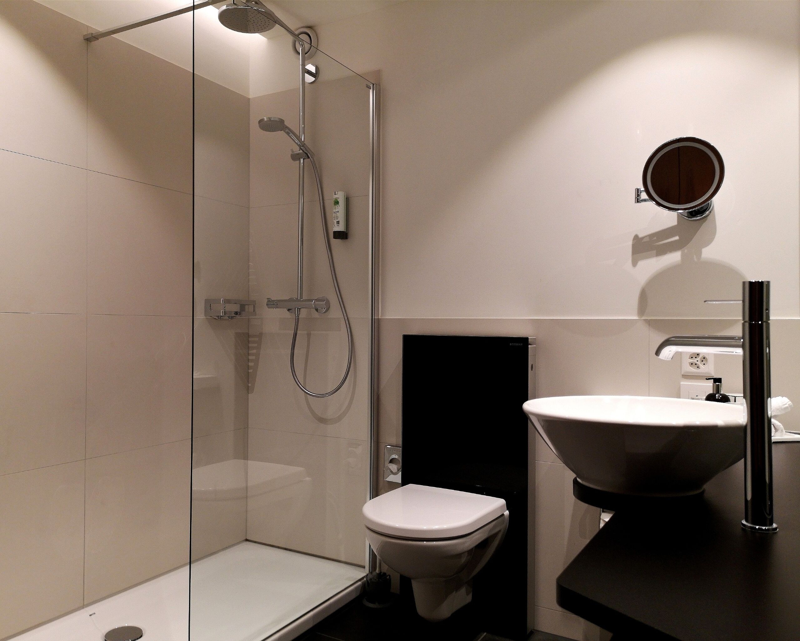 Une salle de bain moderne avec une douche à parois de verre, des toilettes blanches et un lavabo noir.