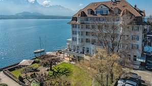A multi-story hotel with balconies overlooking a lake, a dock with boats, and mountains in the background. - Hotel Restaurant Bellevue au Lac (Hilterfingen)