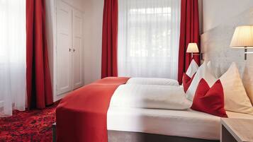 Een hotelkamer met een groot bed, rode gordijnen, een witte kledingkast en een bedlampje.