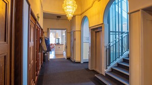 A hallway with wooden paneling, a chandelier, and a staircase with a glass railing. - Hotel Restaurant Bellevue au Lac (Hilterfingen)