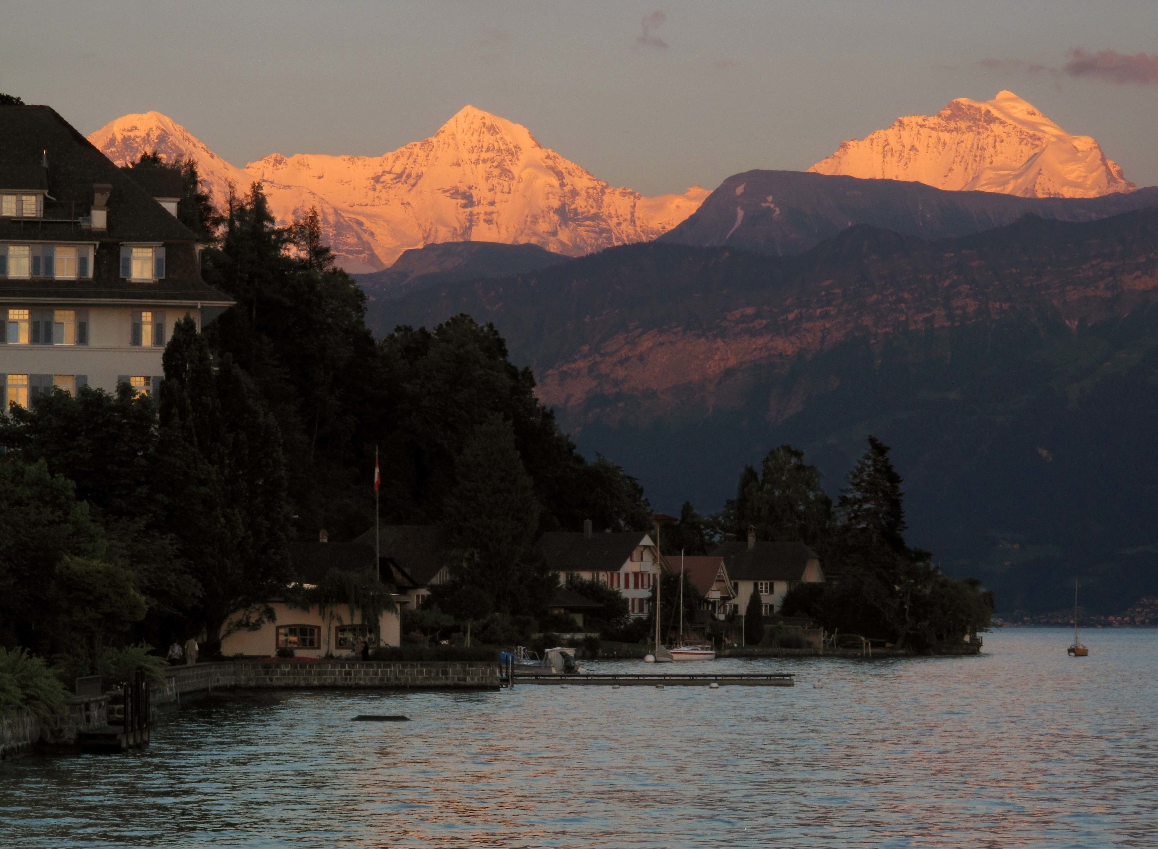 A lakeside view with a mountain in the background and a row of houses along the shore.