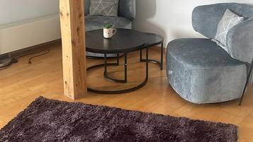 Une pièce avec une poutre en bois, un canapé gris, une table ronde avec une tasse et un tapis foncé.