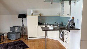 A compact kitchen with white cabinets, a dark countertop, and a small dining area with a chair and a lamp. - Hotel Restaurant Bellevue au Lac (Hilterfingen)