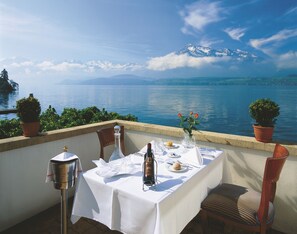 Une table dressée pour deux personnes, avec vue sur un lac et des montagnes en arrière-plan.