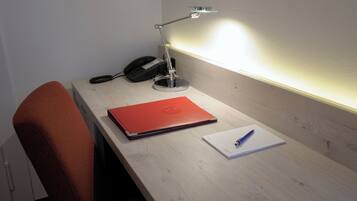 Ein Schreibtisch mit einem Laptop, einem Telefon, einer Lampe und einem Notizbuch.