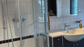 Ein modernes Badezimmer mit einer Duschkabine aus Glas, einem weißen Waschbecken und einem Spiegel darüber.