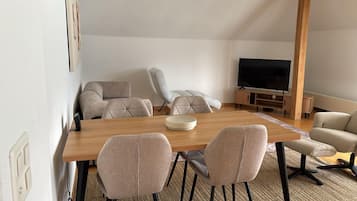 A modern living room with a wooden dining table, six chairs, a sofa, and a TV.