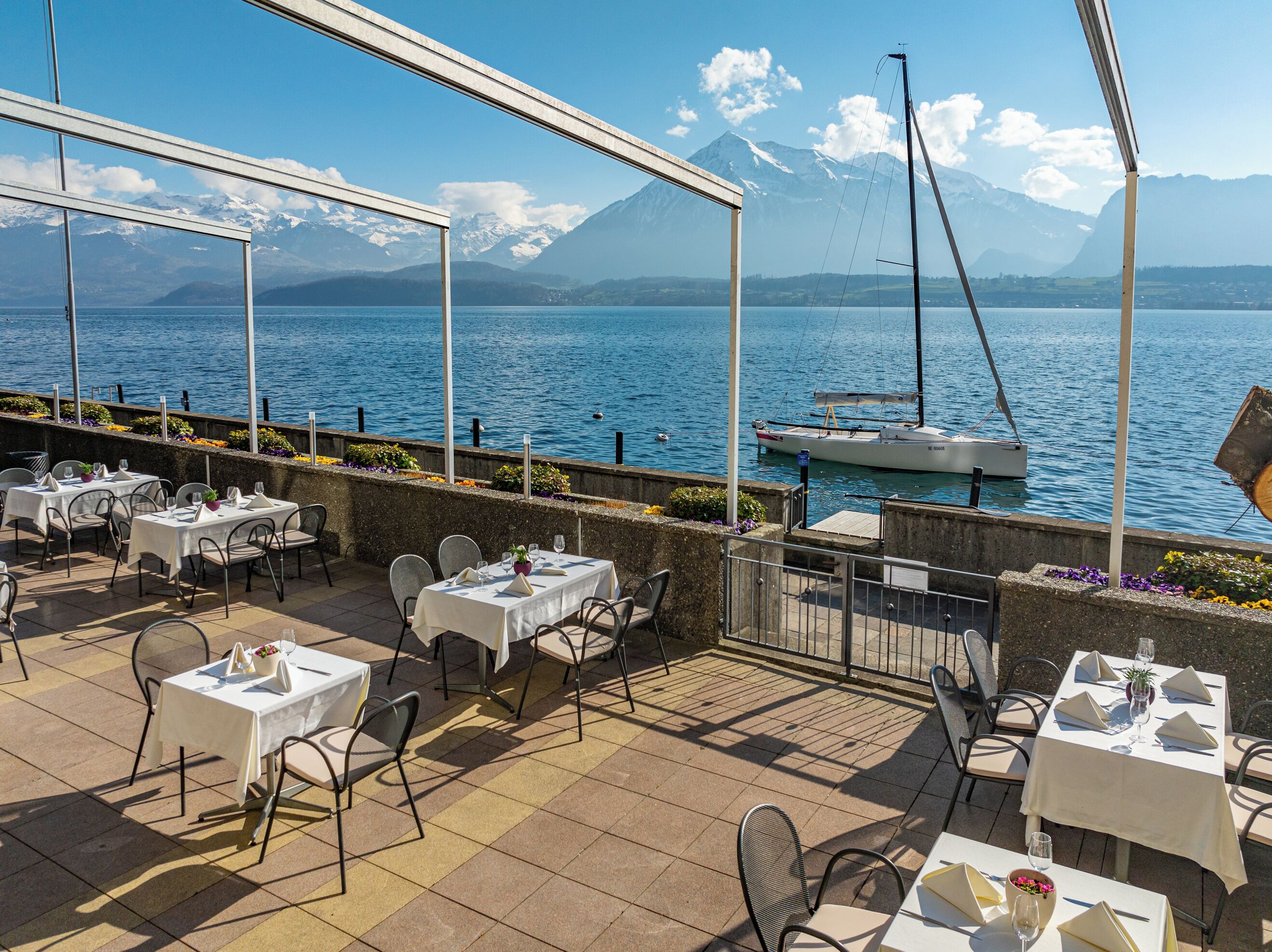An outdoor dining area with tables and chairs, overlooking a body of water and mountains.