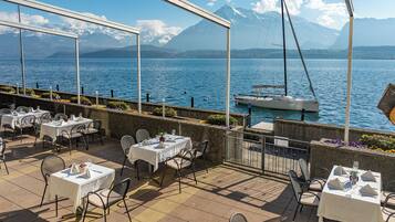 An outdoor dining area with tables and chairs, overlooking a body of water and mountains.