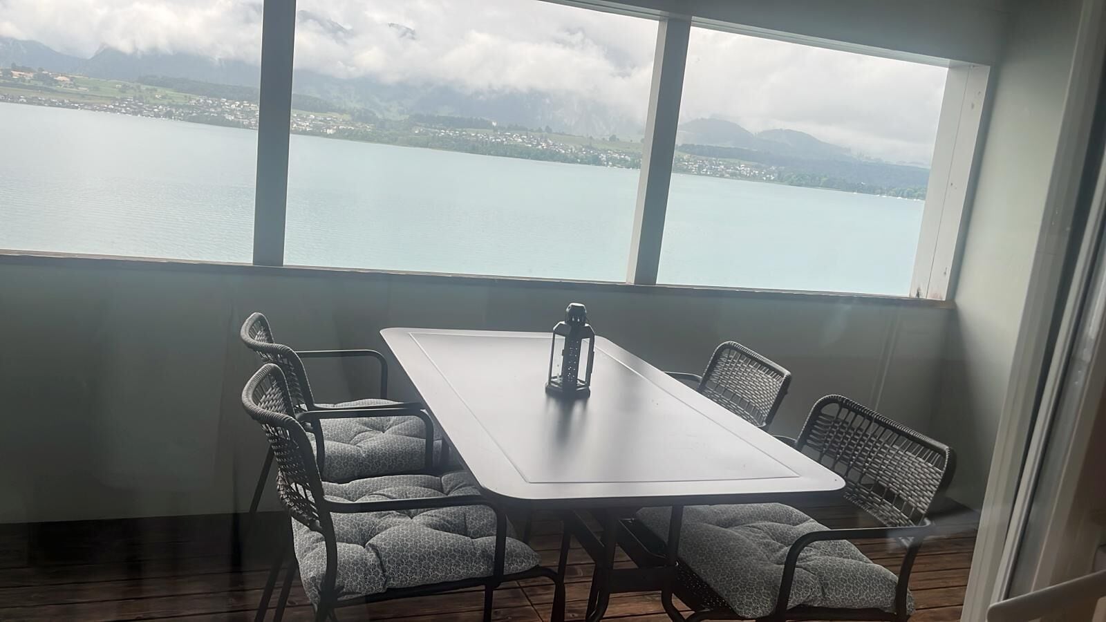 Een eetruimte met een tafel en stoelen, grote ramen met uitzicht op een meer en bergen, en een houten vloer.