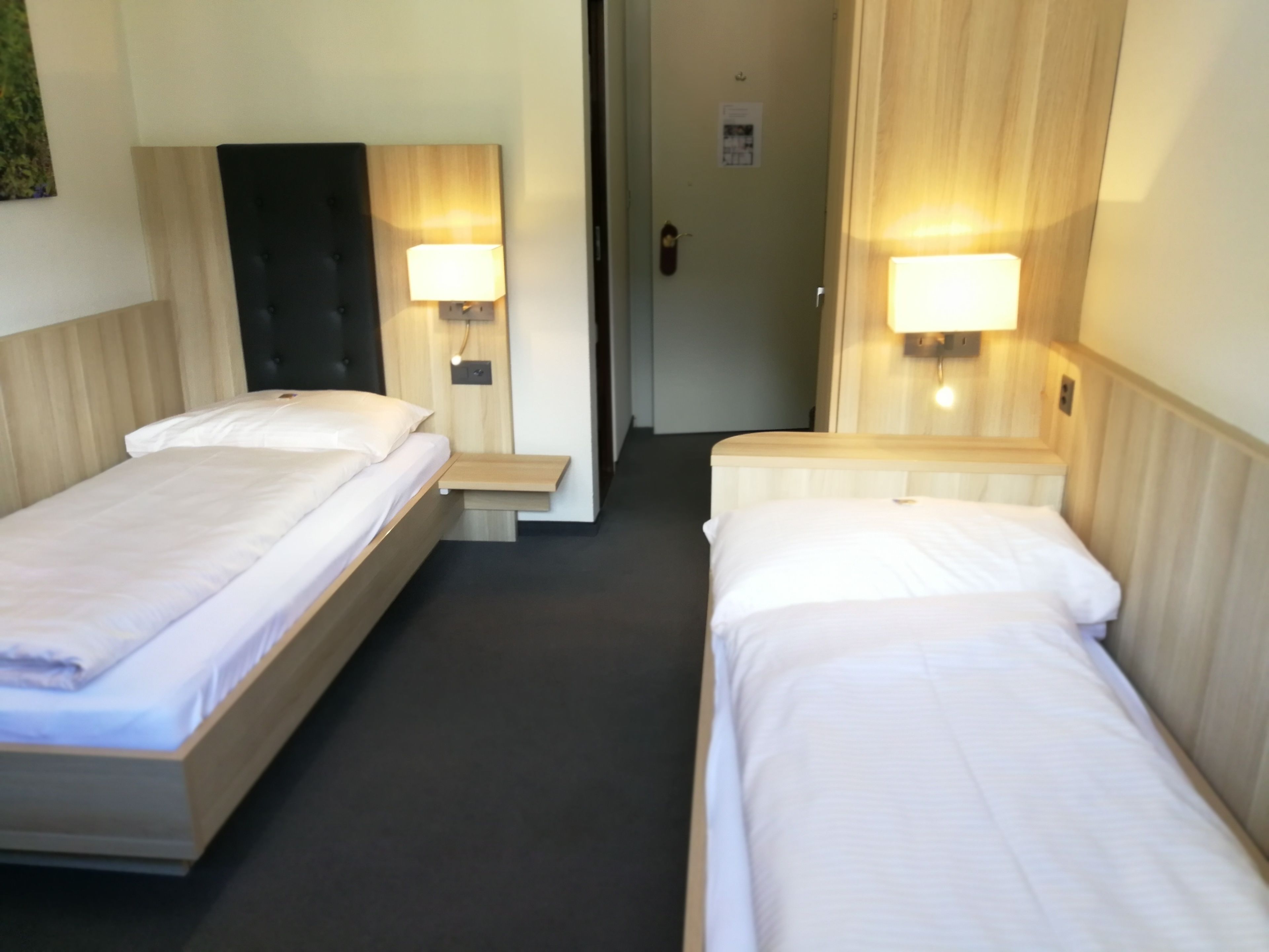 Una habitación de hotel con dos camas individuales, cada una con cabecero de madera y una mesita de noche con lámpara.