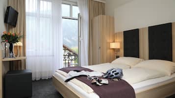 Ein Hotelzimmer mit einem Bett, einem Fernseher, einem Schreibtisch und einem Fenster mit Vorhängen.
