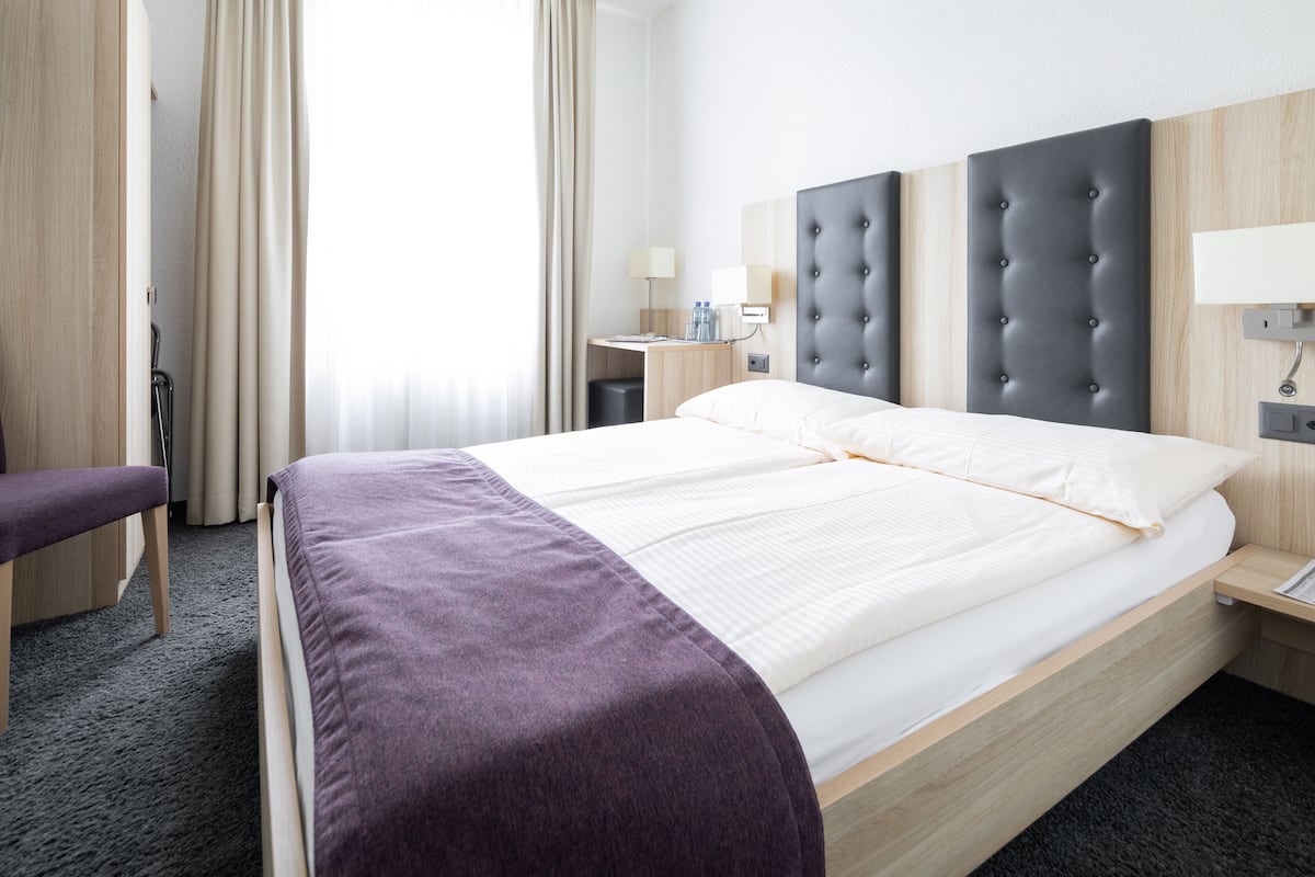 Habitación de hotel con cama, escritorio, silla y ventana con cortinas.