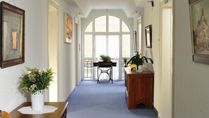 Un couloir avec un tapis bleu, des meubles en bois et des œuvres d’art encadrées accrochées aux murs.