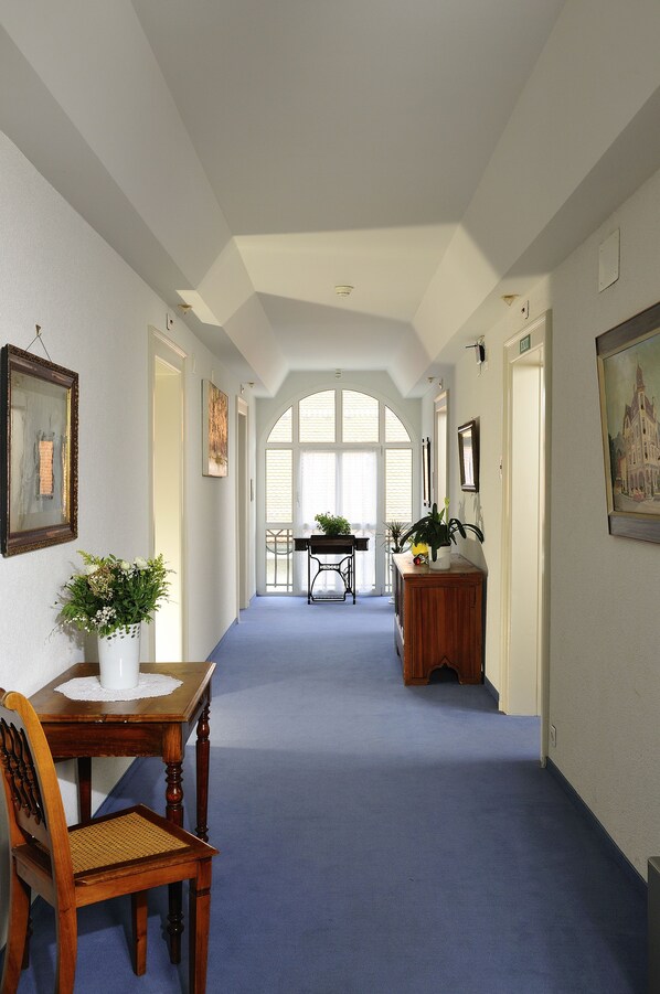 A hallway with a blue carpet, wooden furniture, and framed artwork on the walls. - Hotel Lötschberg (Interlaken)