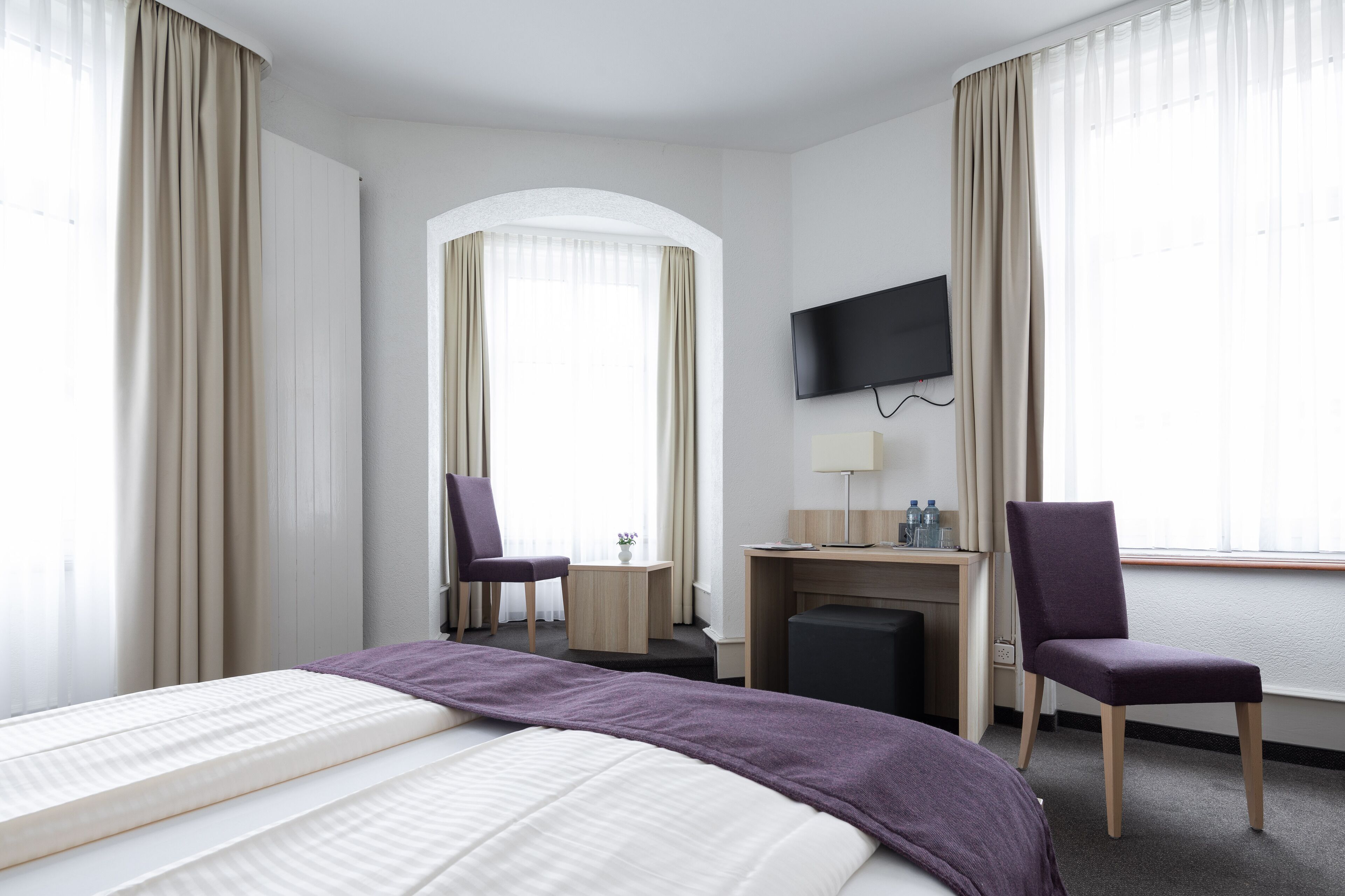 A hotel room with a bed, two chairs, a desk, a television, and a fireplace.