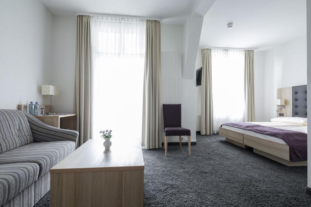 Ein Hotelzimmer mit einer Couch, einem Schreibtisch, einem Sessel, einem Bett und einem an der Wand befestigten Fernseher.
