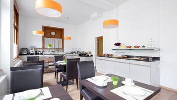 Un comedor moderno con una mesa y sillas de madera, una cocina al fondo e iluminación colgante.