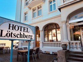 Un letrero de hotel con 'HOTEL LÖTSCHBERG' frente a un edificio de arquitectura clásica.