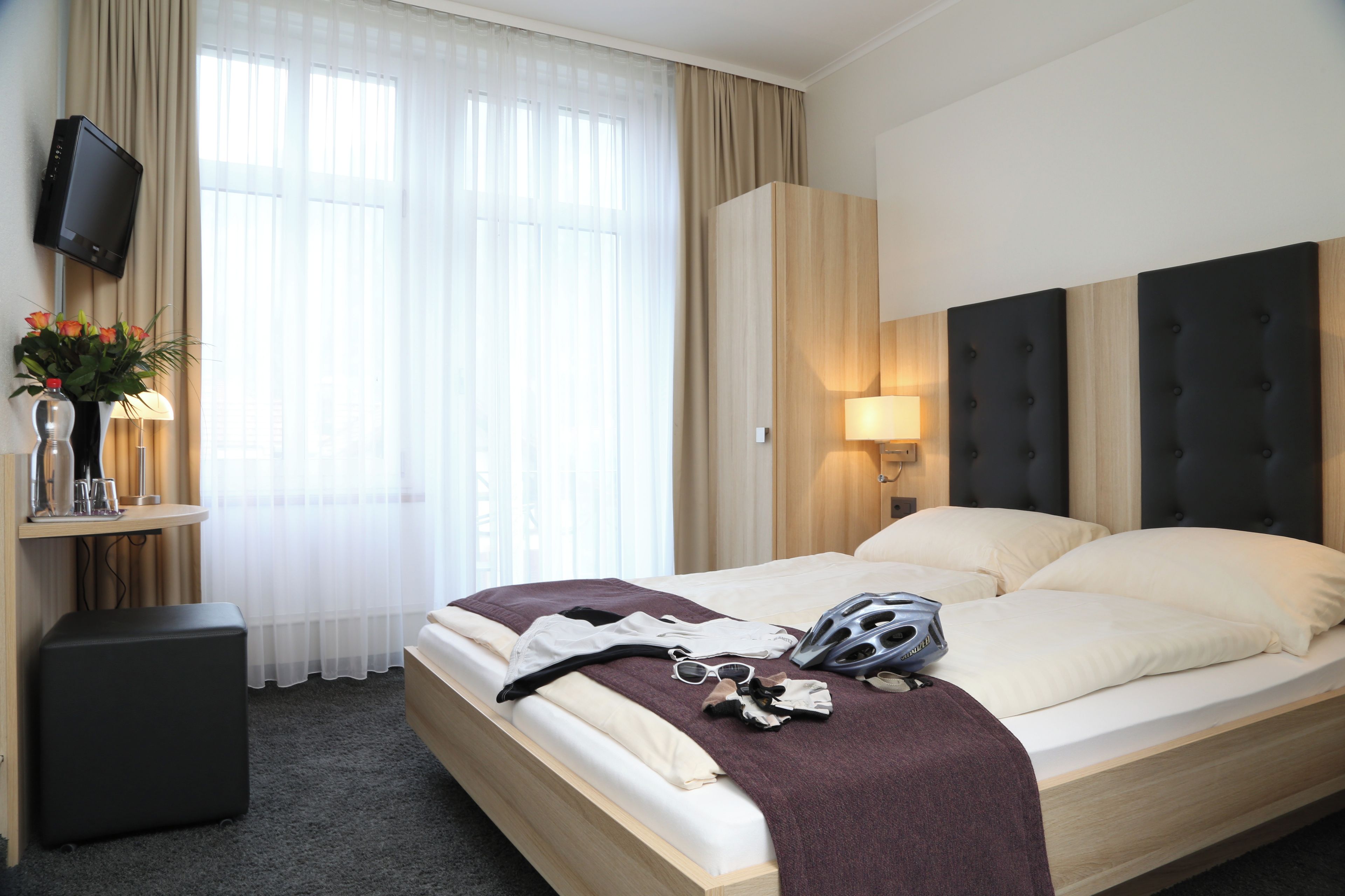 Una habitación de hotel con una cama, televisión, lámpara y ventana con cortinas.