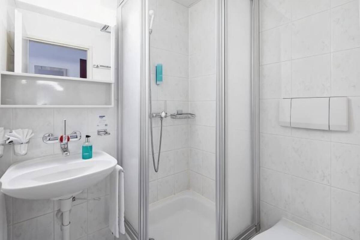 Un baño con ducha de vidrio, un lavamanos blanco y un espejo sobre él.