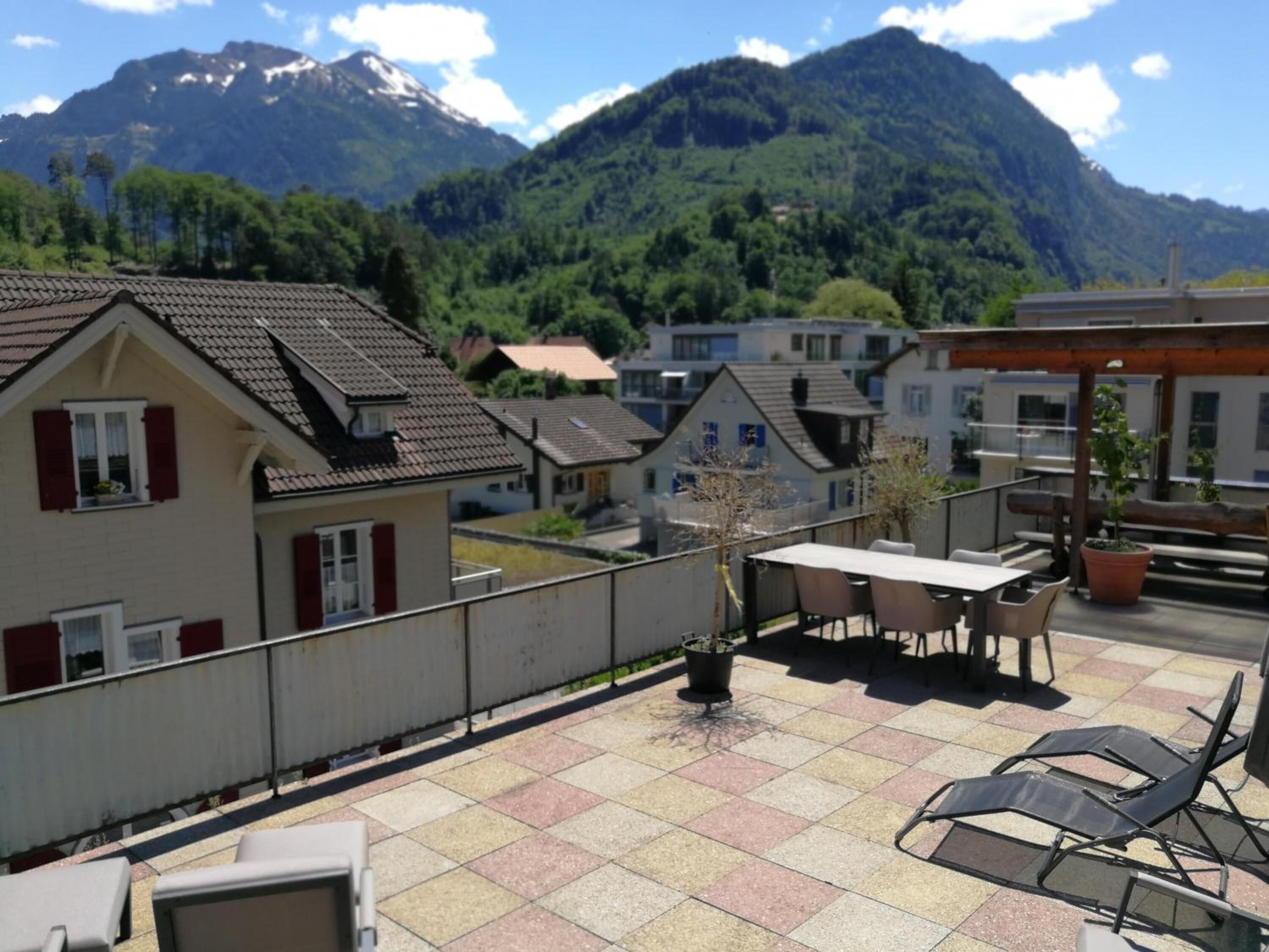 Una terraza en la azotea con una mesa, sillas, una planta en maceta y vistas a una cordillera.