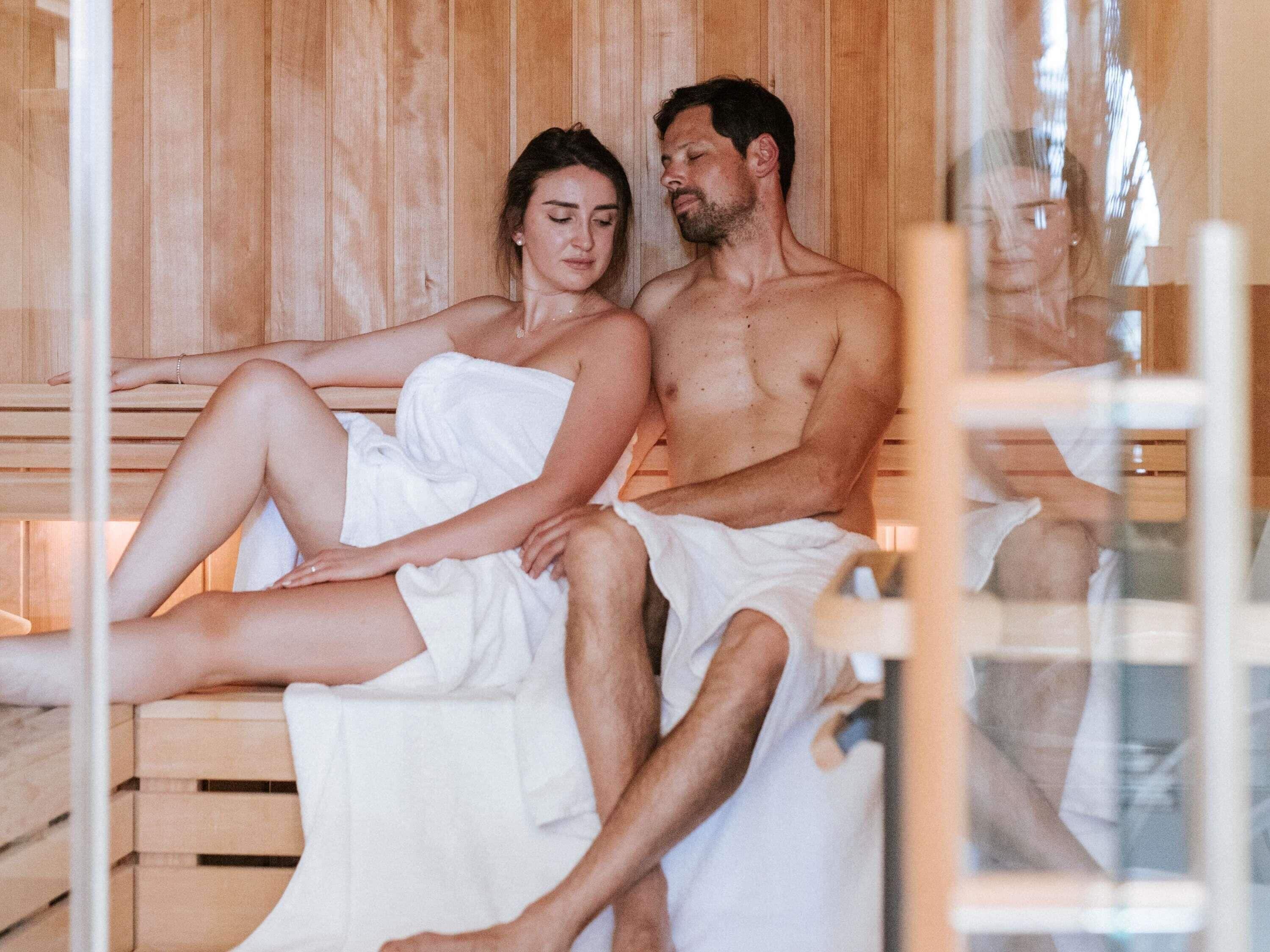 A couple in a sauna with wooden walls and benches.
