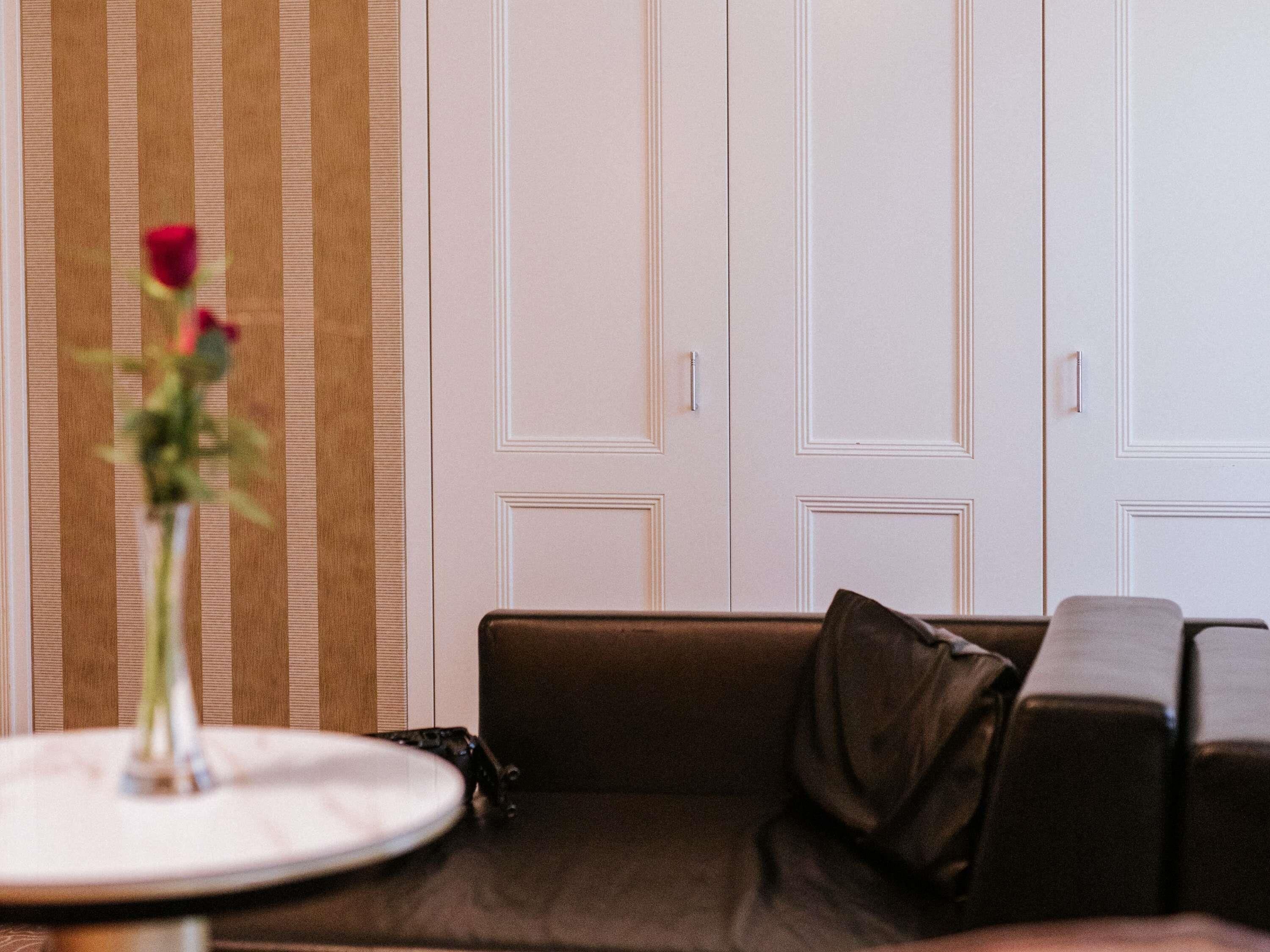 Une pièce avec un canapé marron, une table ronde ornée d’un vase de fleurs et une porte blanche à panneaux.