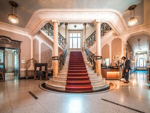 Un magnifique escalier orné de balustrades travaillées, un comptoir d’accueil et un sol en marbre poli.