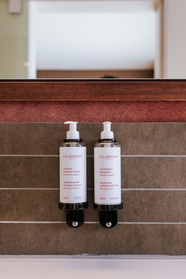 Twee Clarins Paris huidverzorgingsflessen bevestigd aan een betegelde muur.