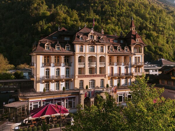 Un grand hôtel historique doté de nombreux balcons et d’une tour imposante, entouré d’une végétation luxuriante.