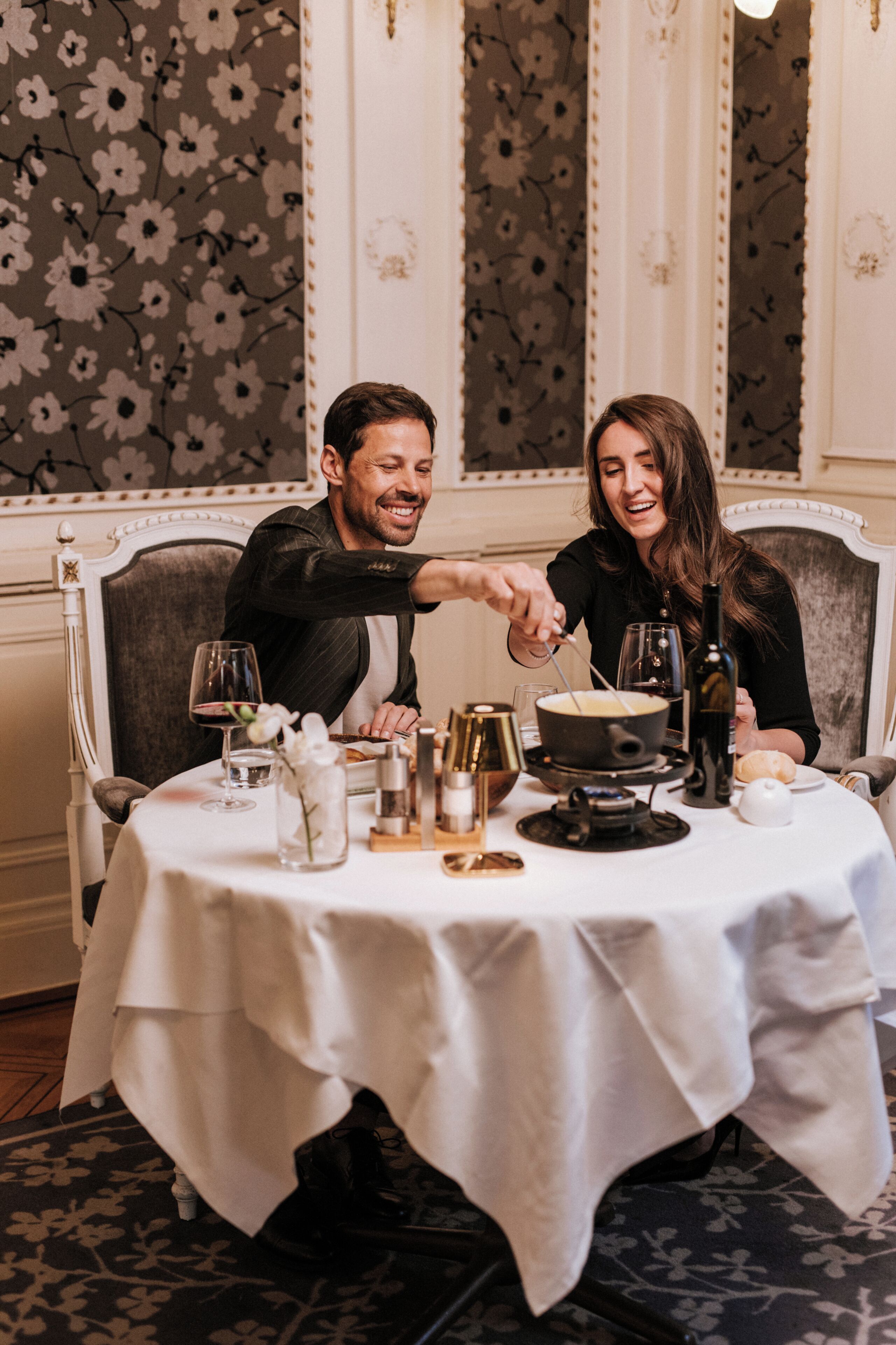 Una mesa de comedor con mantel blanco, un tazón de sopa, copas de vino y una botella de vino.