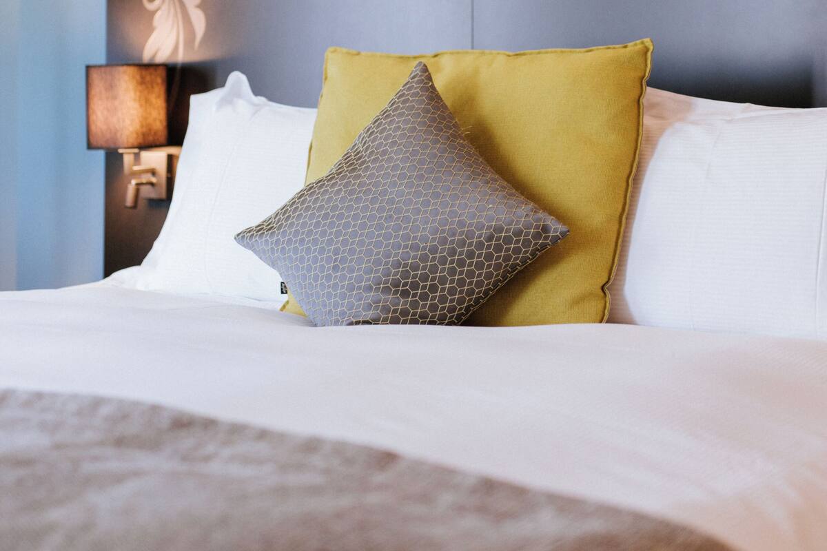 A neatly made bed with a variety of pillows, a wall-mounted lamp, and a decorative headboard with a crown emblem.