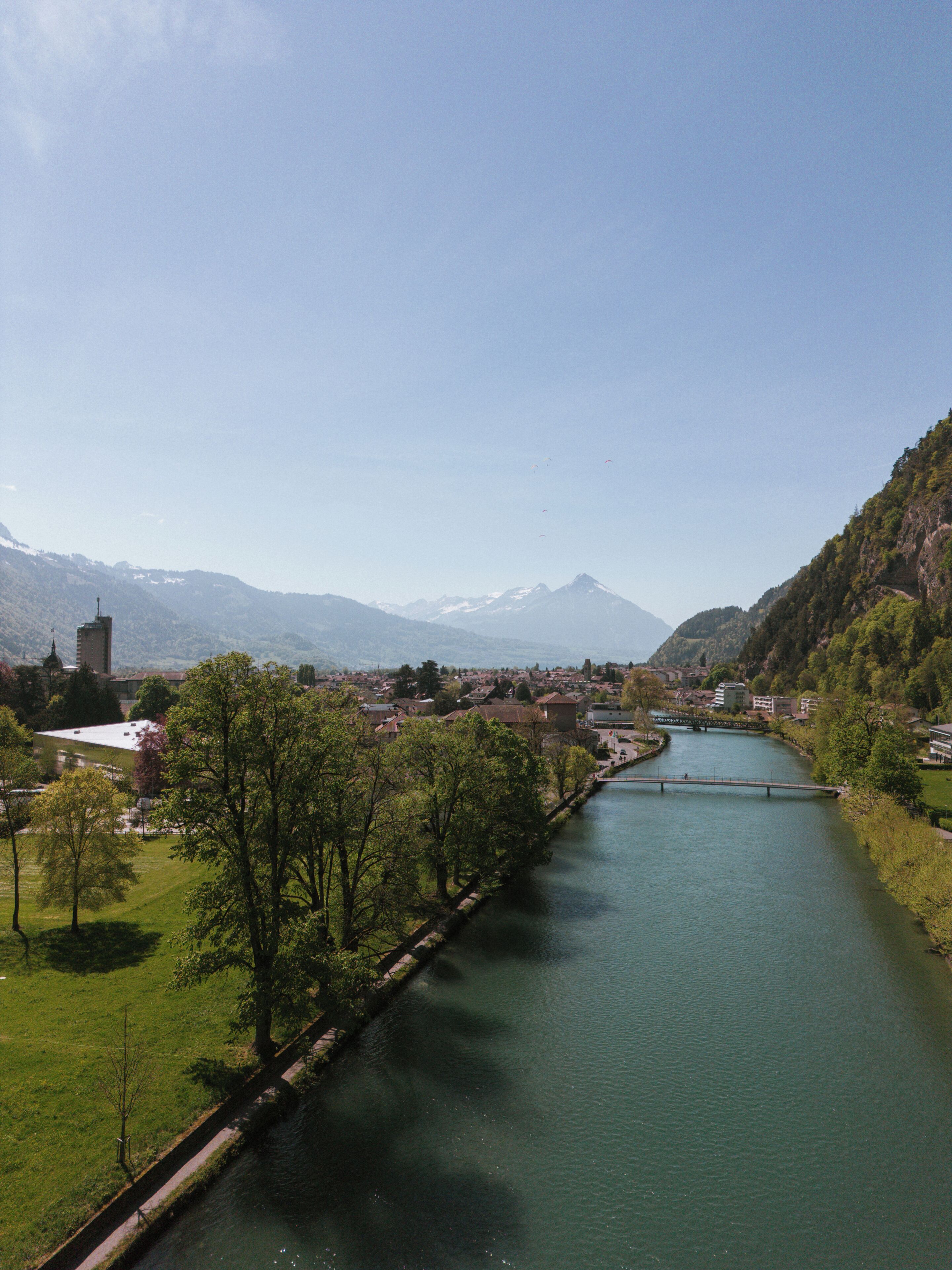 A river with a bridge, surrounded by greenery and mountains.