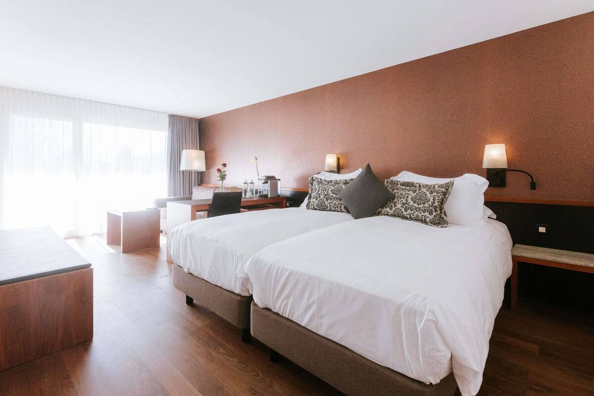 A hotel room with a large bed, bedside tables, a desk, and a lamp.
