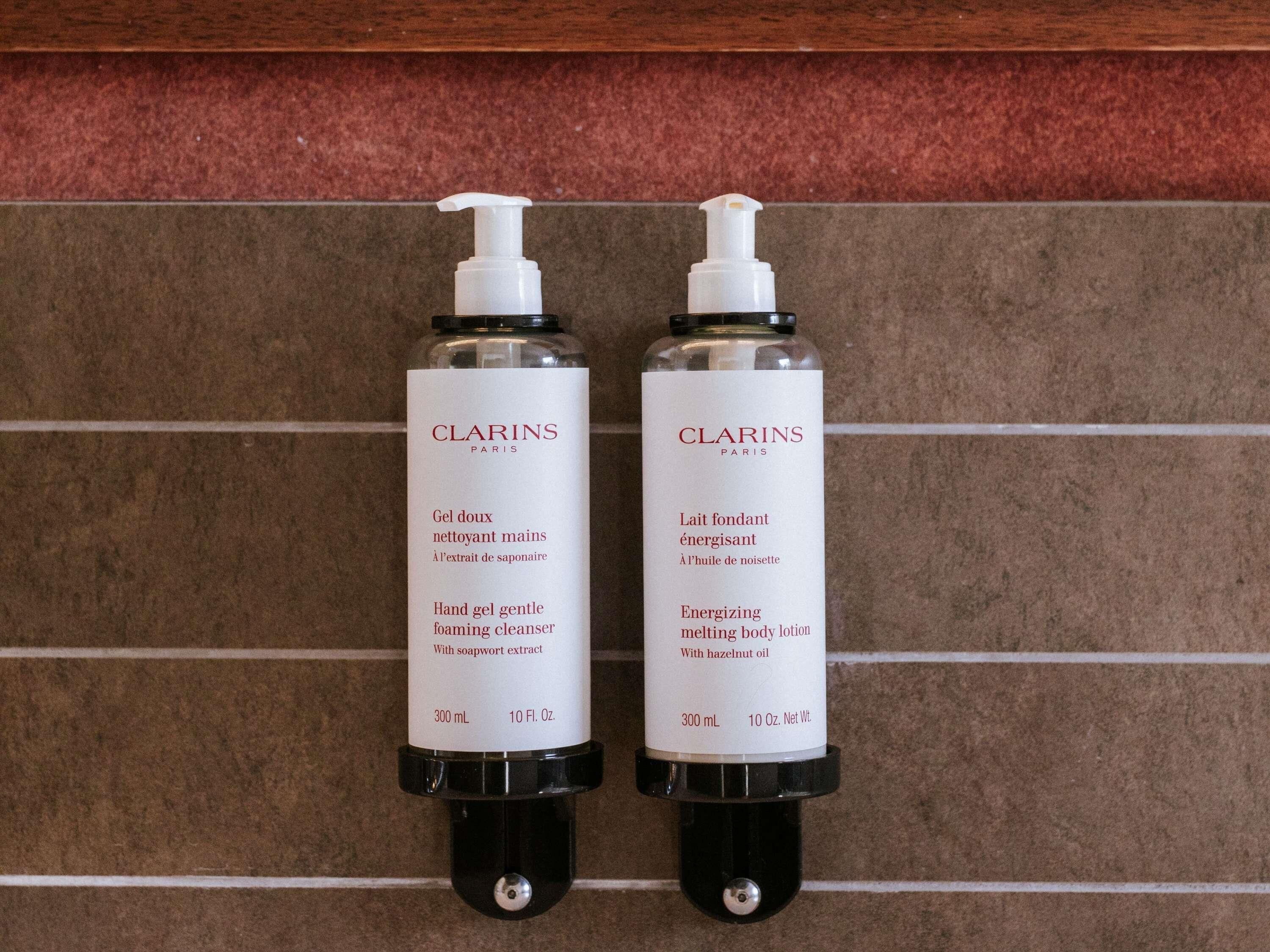 Two Clarins Paris hand gel bottles on a tiled wall.