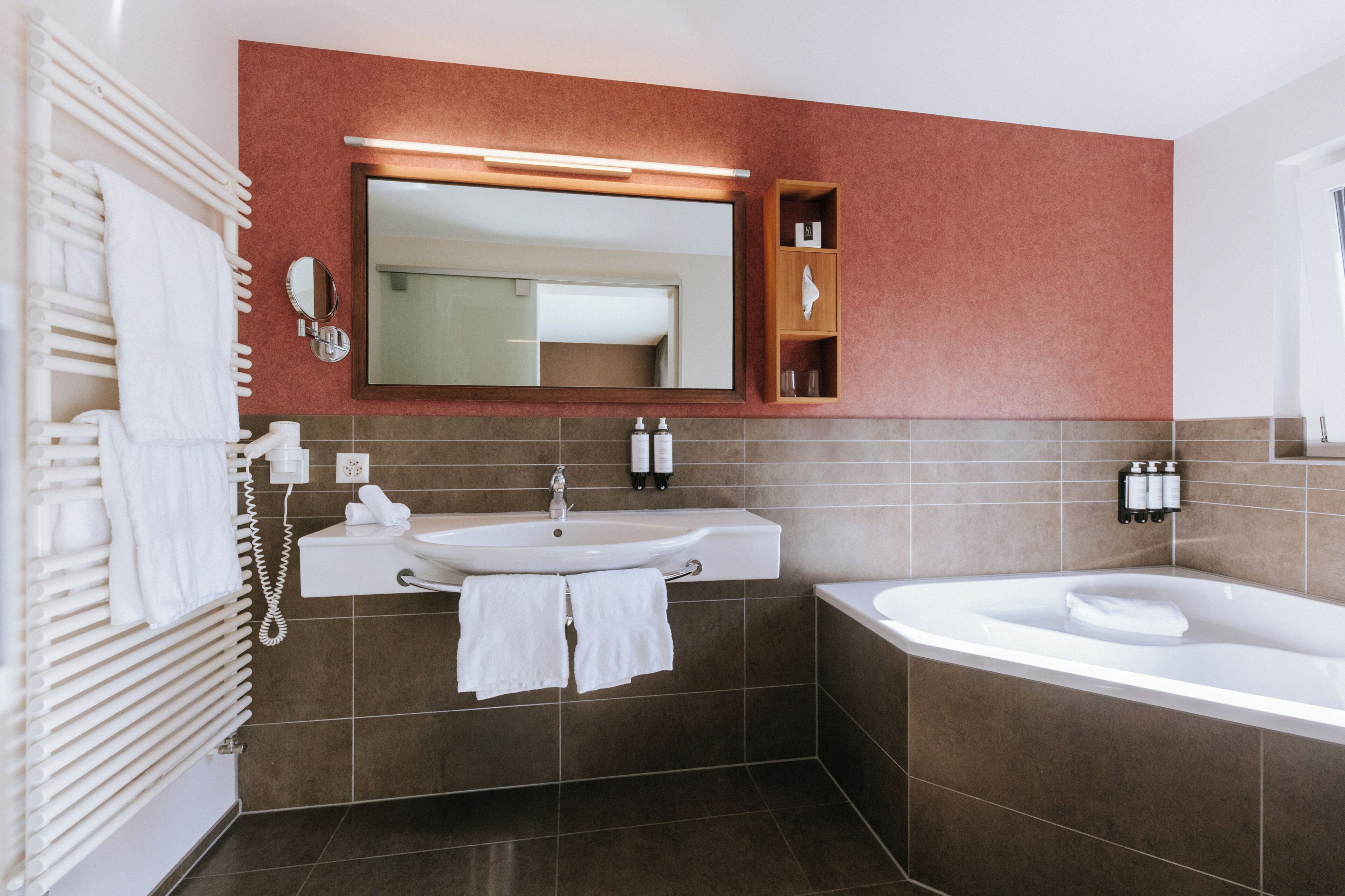 A modern bathroom with a white sink, a large mirror, a bathtub, and a towel rack.