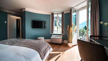 A modern hotel room with a large bed, a flat-screen TV, a small seating area, and a balcony with a view.