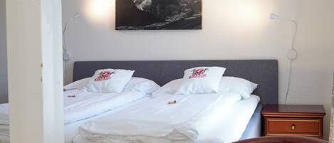 A neatly made bed with white linens and pillows, a gray headboard, and a mountain landscape painting above it.