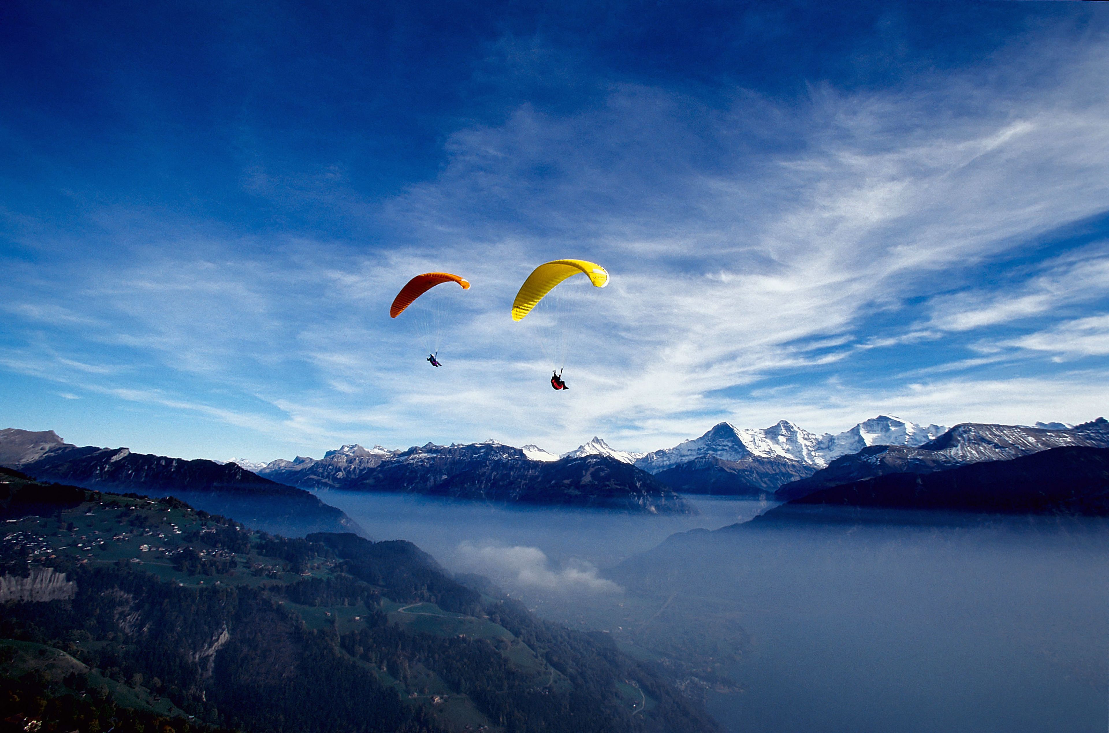 Un paysage montagneux, avec un ciel dégagé et deux parachutes visibles.
