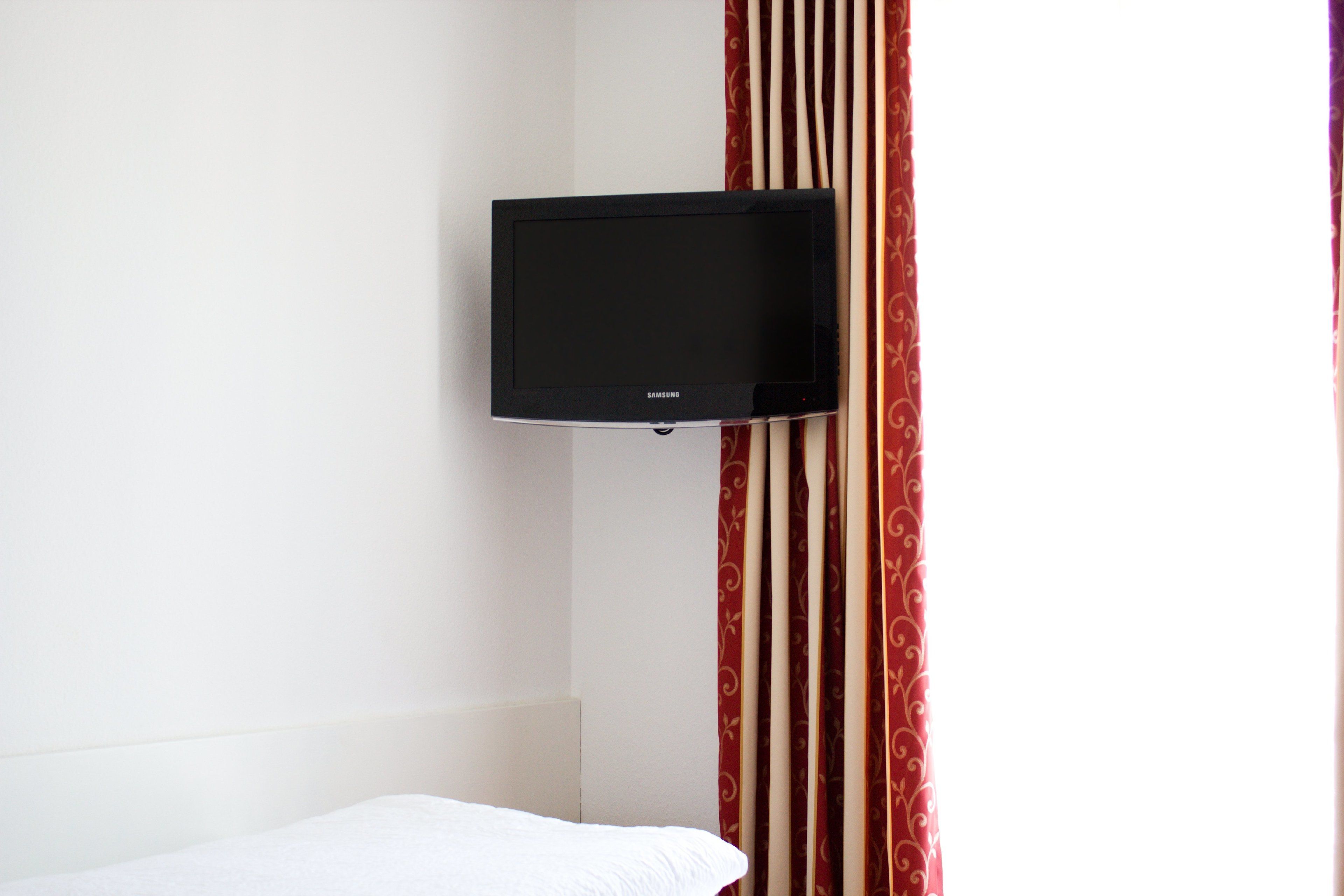 A room with a bed, a wall-mounted television, and a curtain with a pattern.