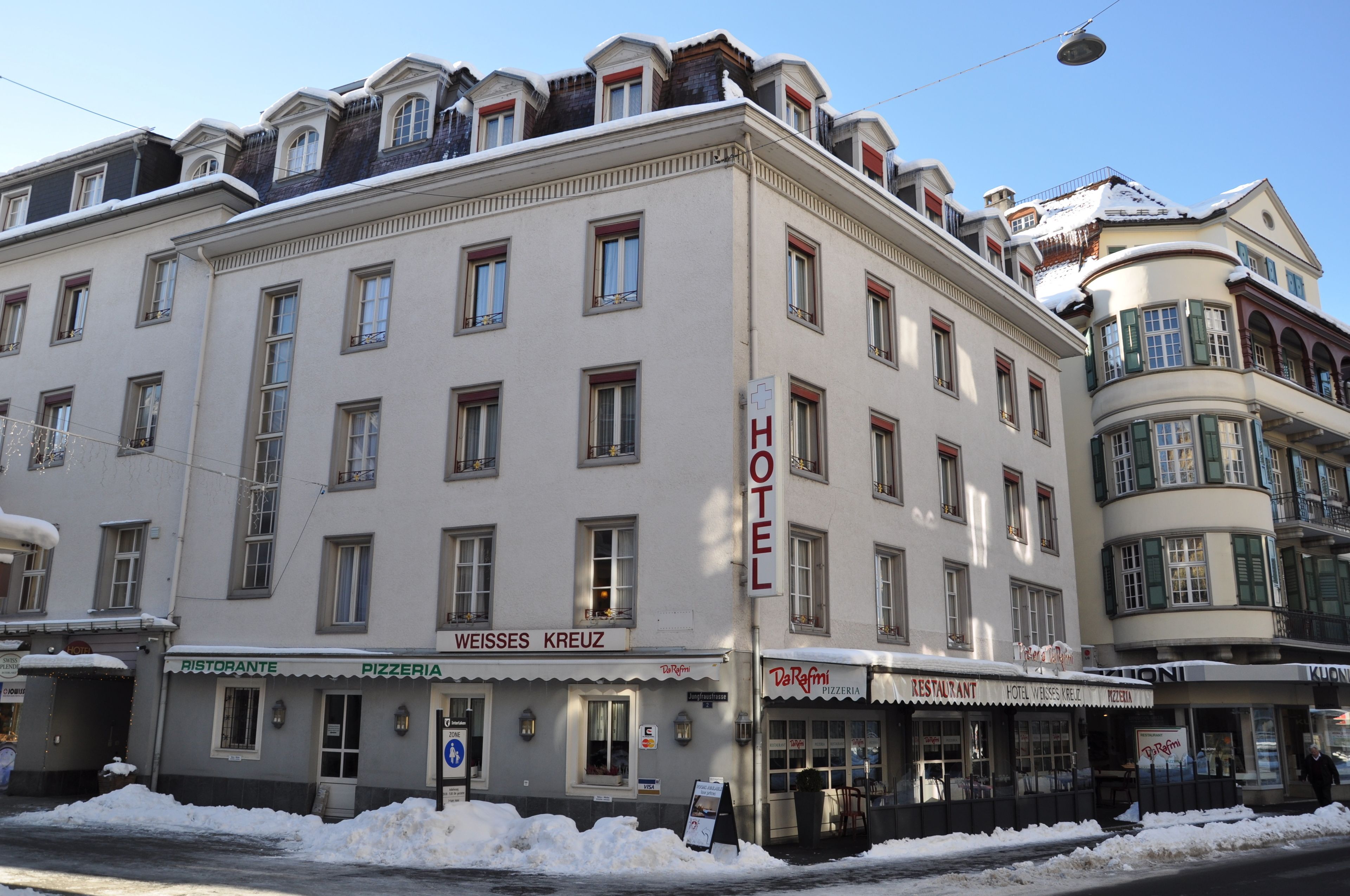 A hotel with a sign indicating it offers a restaurant, pizzeria, and a hotel named Weiss Kreuz.