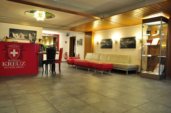 A hotel lobby with a reception desk, seating area, and a display of wine bottles. - Hotel Weisses Kreuz (Interlaken)