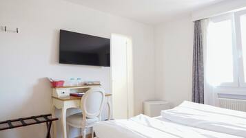 A hotel room with a bed, a desk with a chair, a television mounted on the wall, and a window with curtains.