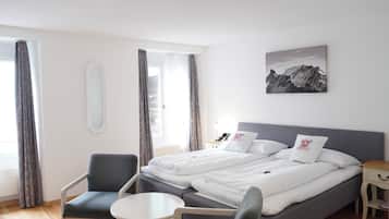 A hotel room with a bed, two chairs, a small table, a bedside table, a mirror, and a picture on the wall.