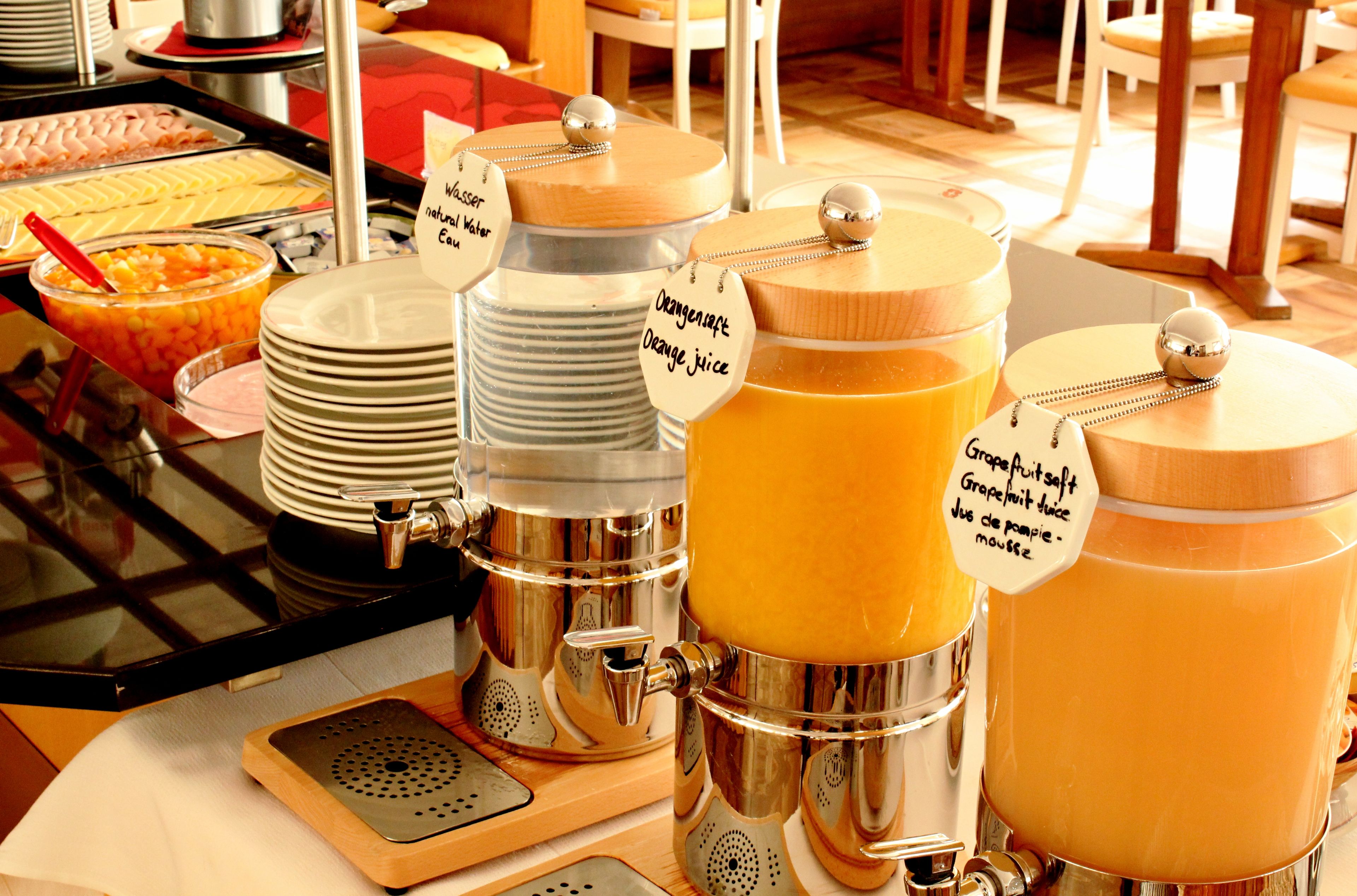 Una mesa de buffet con diferentes dispensadores de comida y bebida, incluyendo jugo de naranja y jugo de toronja.