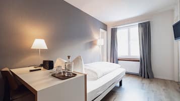 Una habitación de hotel con una cama, un escritorio con lámpara, una botella y una cámara.